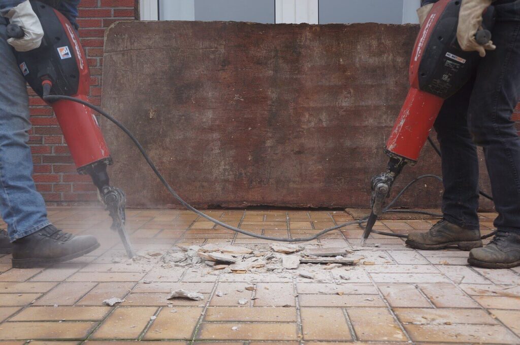 two workers using jackhammers to break down tiling